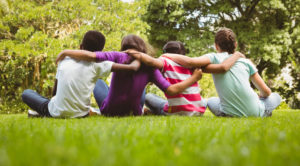 Group of kids sitting in the grass with their arms around each other.